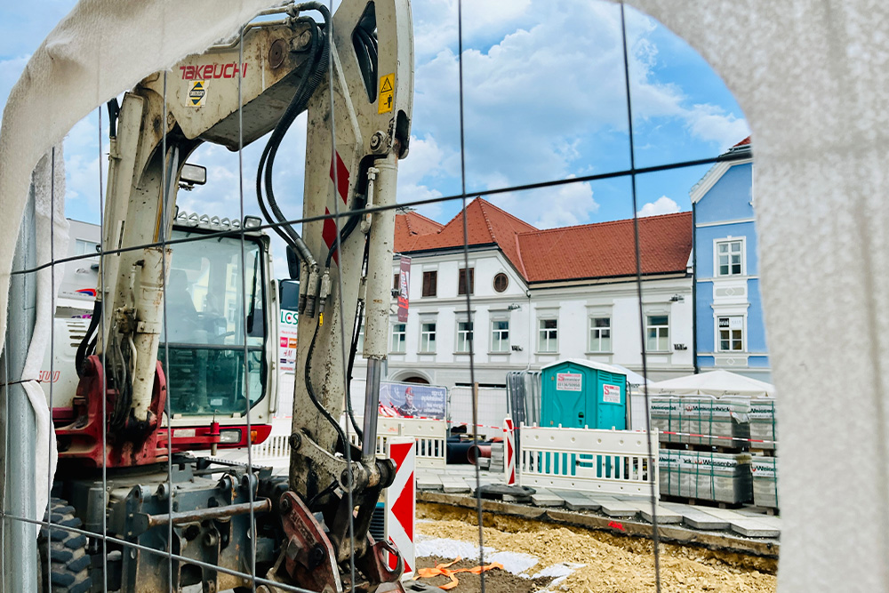 Blick durch Baustellengitter auf Detailaufnahme von Bagger